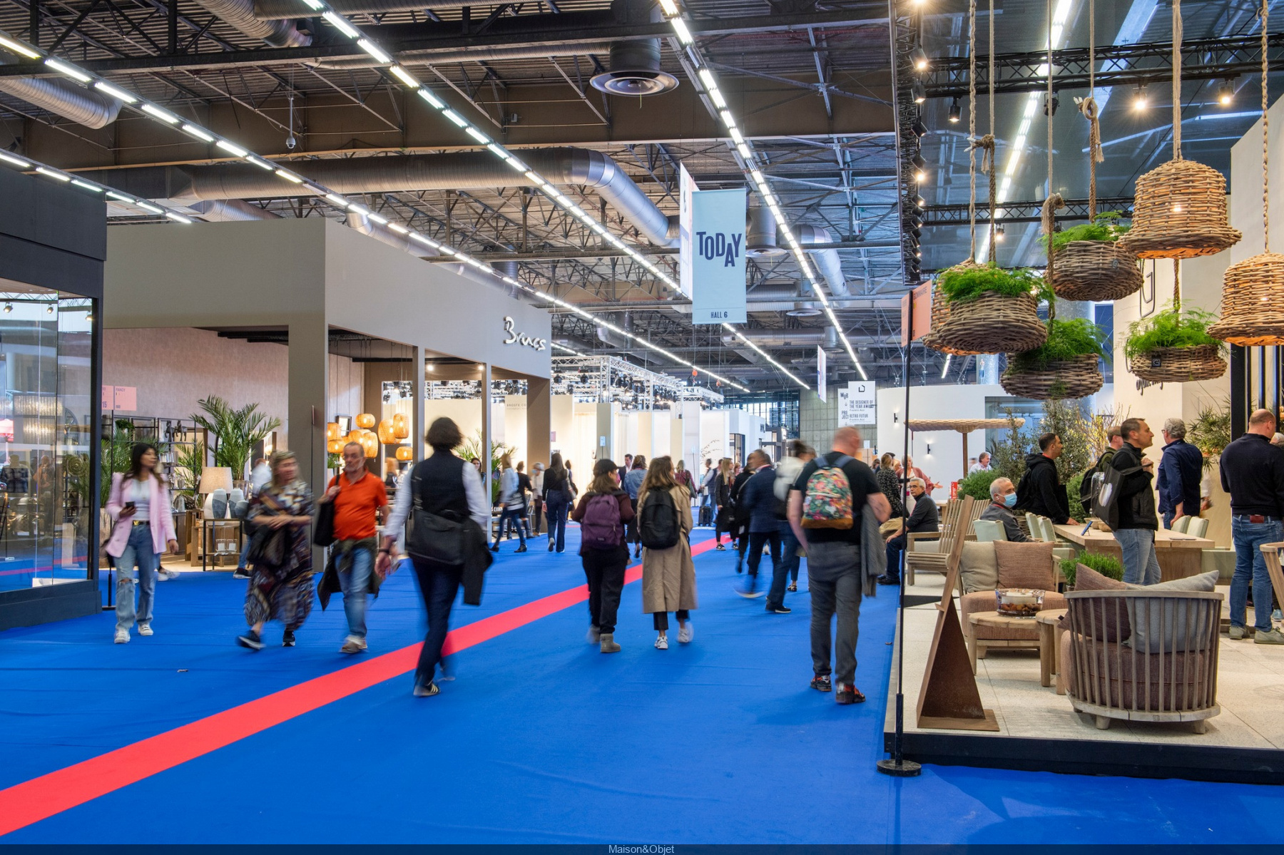 The image captures a bustling interior design fair with attendees exploring exhibition booths featuring stylish furniture, lighting, and décor. The event provides a dynamic space for networking and showcasing the latest design trends. - Nolita Harbour 