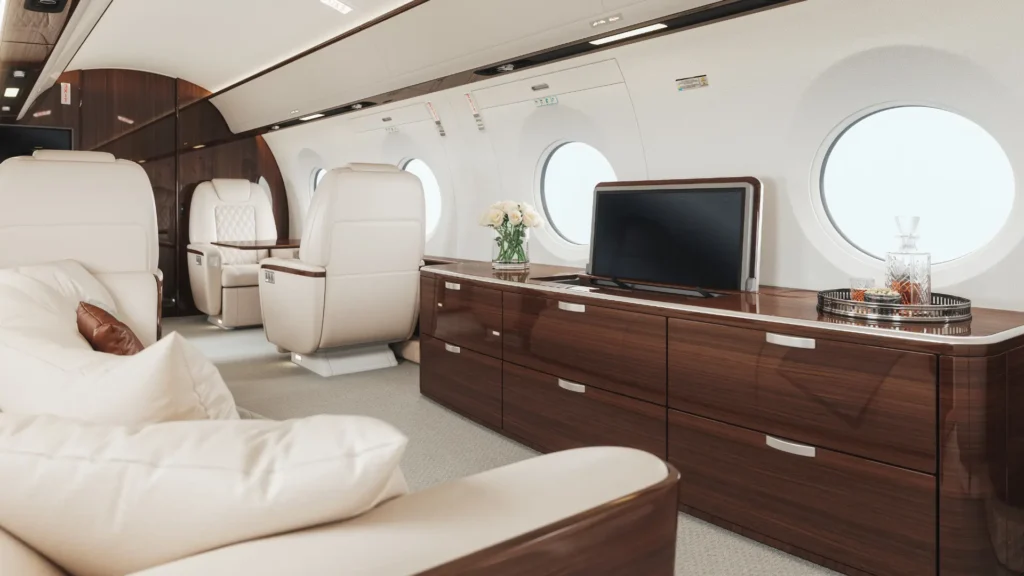 Luxurious private jet interior with cream leather seating, wood paneling, flat-screen TV, and drinks tray by round windows.