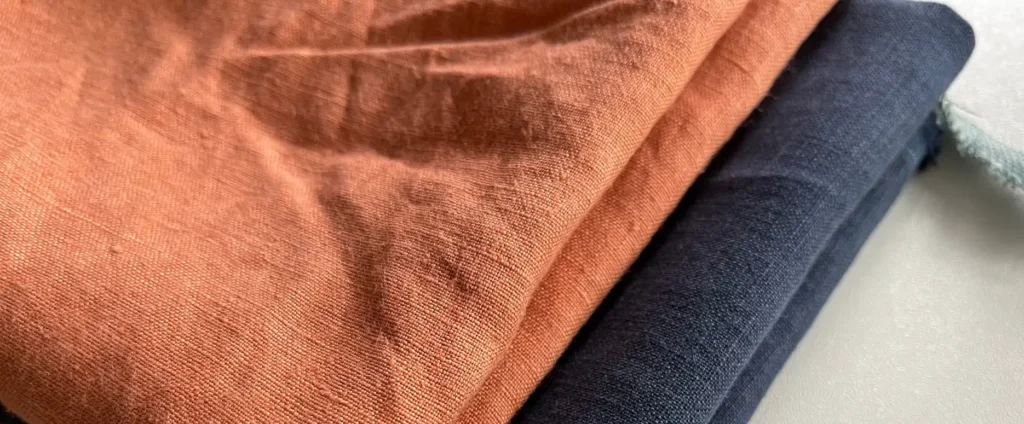 Close-up of folded linen fabrics in terracotta orange and deep navy blue tones on a light surface.
