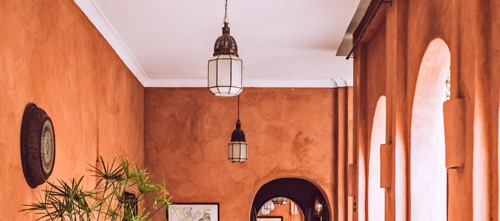 Mediterranean-style hallway with terracotta walls, arched windows, rustic wooden furniture, and potted plants.