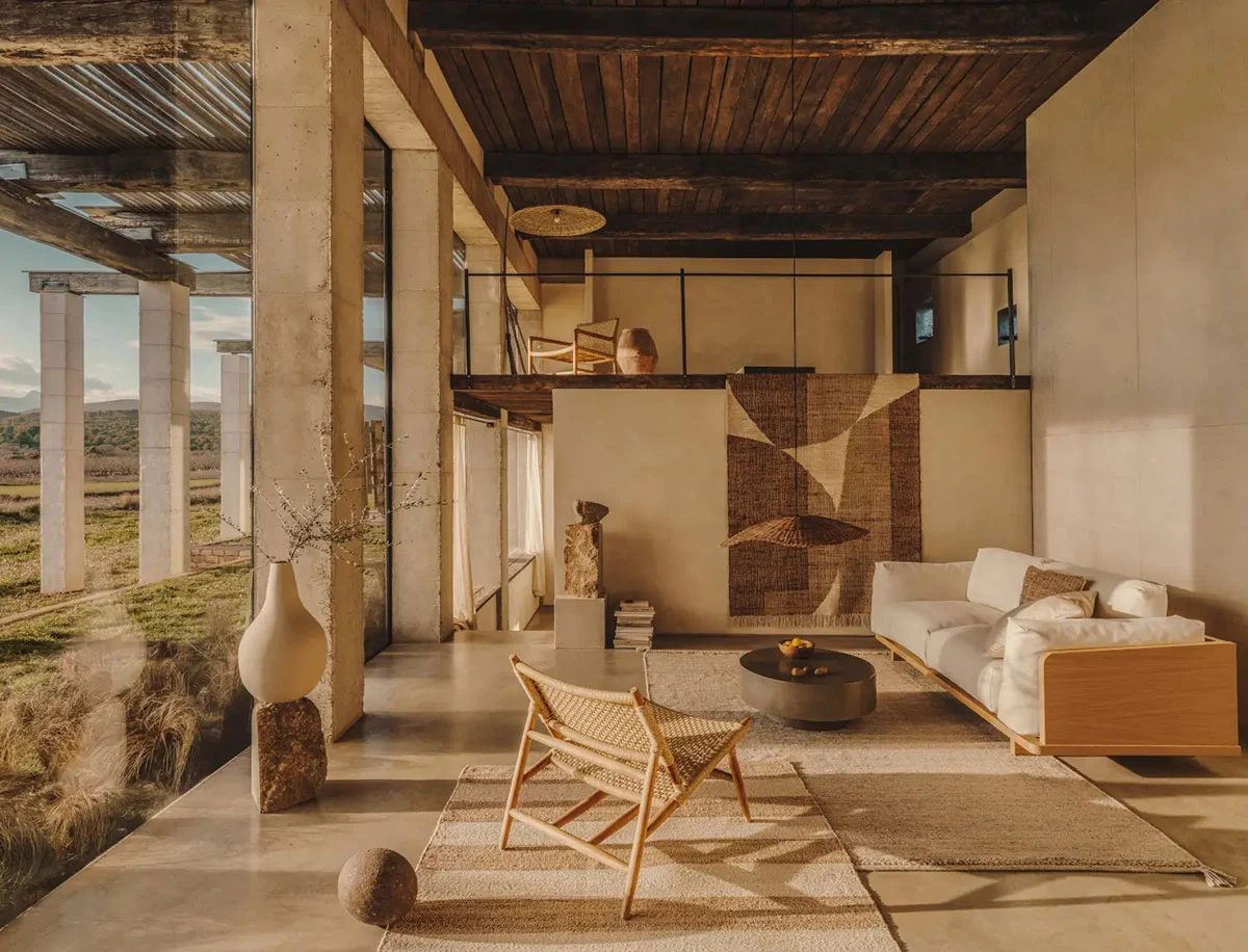 Modern Mediterranean Interior Design living room with high ceilings, natural stone walls, minimalist furniture, and large windows overlooking the landscape