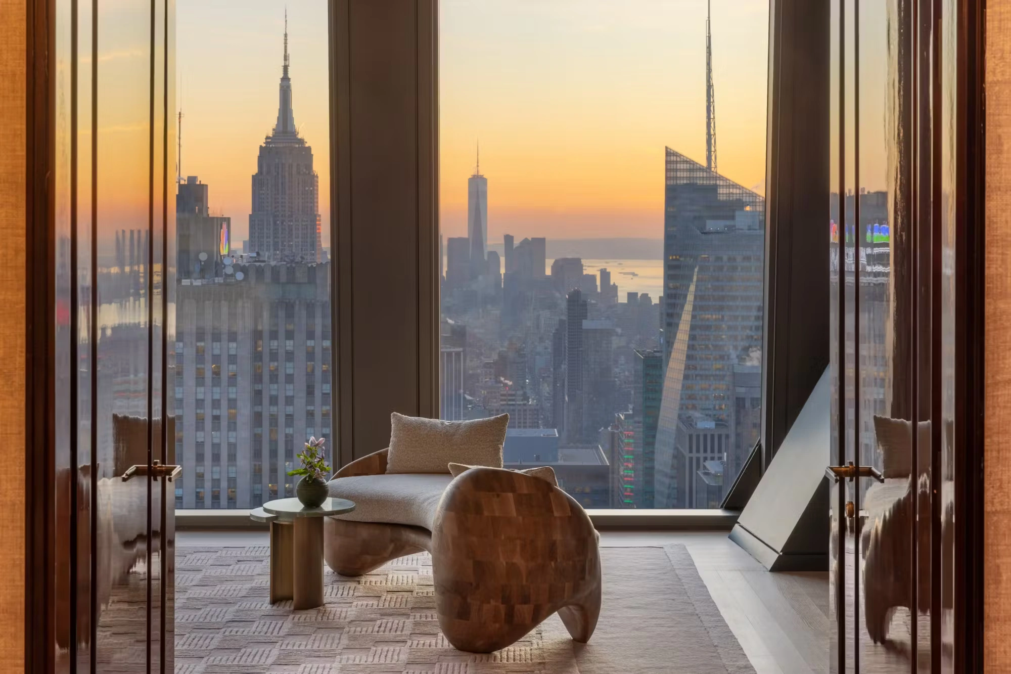 New York penthouse lounge with Empire State Building views, floor-to-ceiling glazing, sculptural seating, and serene luxury interior design emphasizing vertical living.