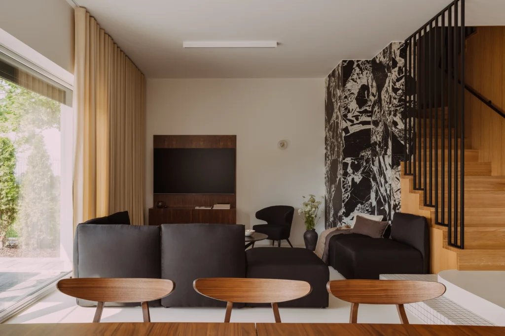 Modern living room interior featuring a dramatic black marble accent wall, walnut furniture, and soft neutral seating, illustrating the balance of marble and wood in luxury interiors.