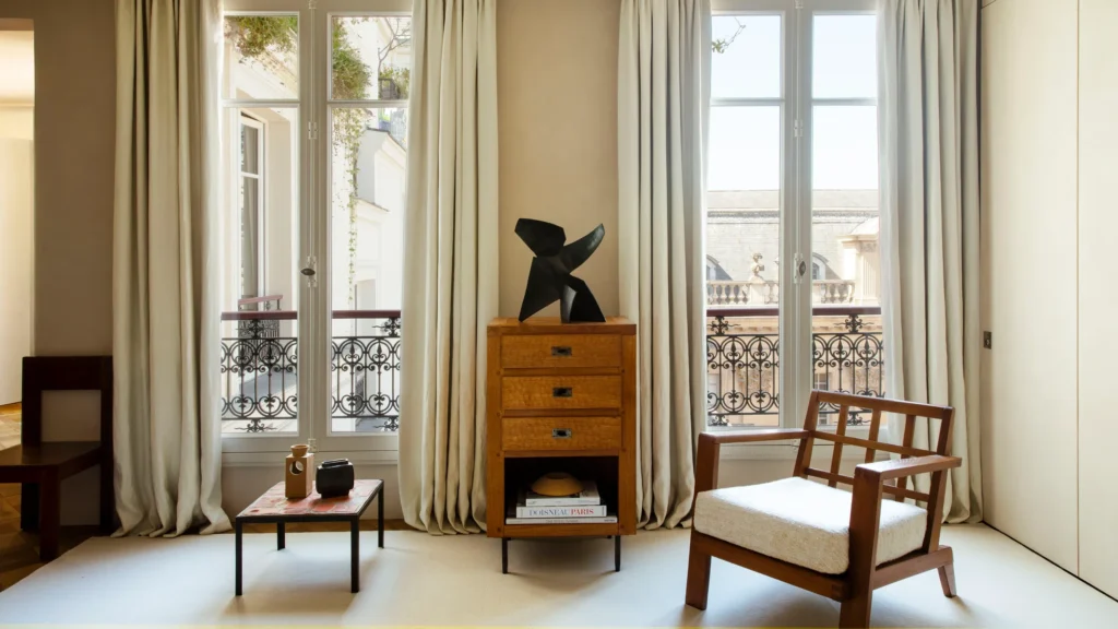 Parisian luxury interior with tall French windows, sculptural furniture, and restrained material palette, blending architectural minimalism with classic urban elegance.