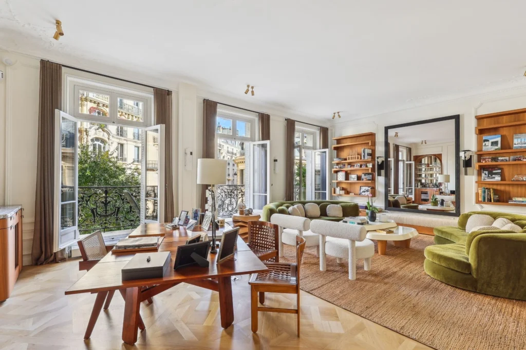 Light-filled Parisian apartment design with herringbone parquet floors, open-plan living and dining areas, custom wood furniture, and large French windows overlooking classic Parisian balconies