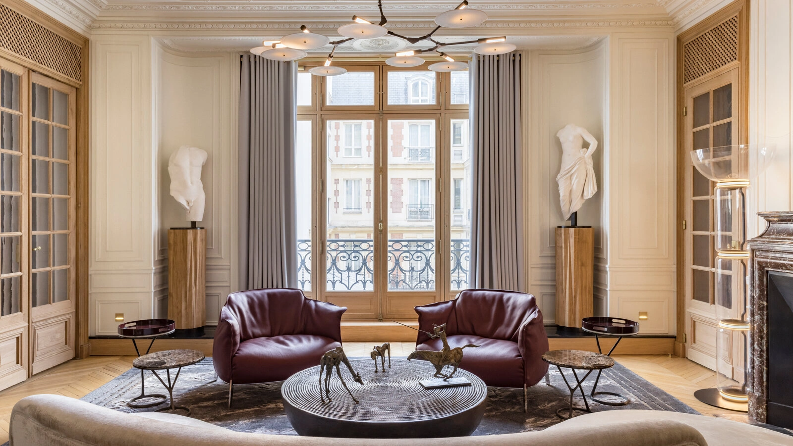 Refined Parisian apartment living room featuring restored Haussmann moldings, tall French windows, sculptural contemporary seating, and a balanced dialogue between classical architecture and modern urban interior design.