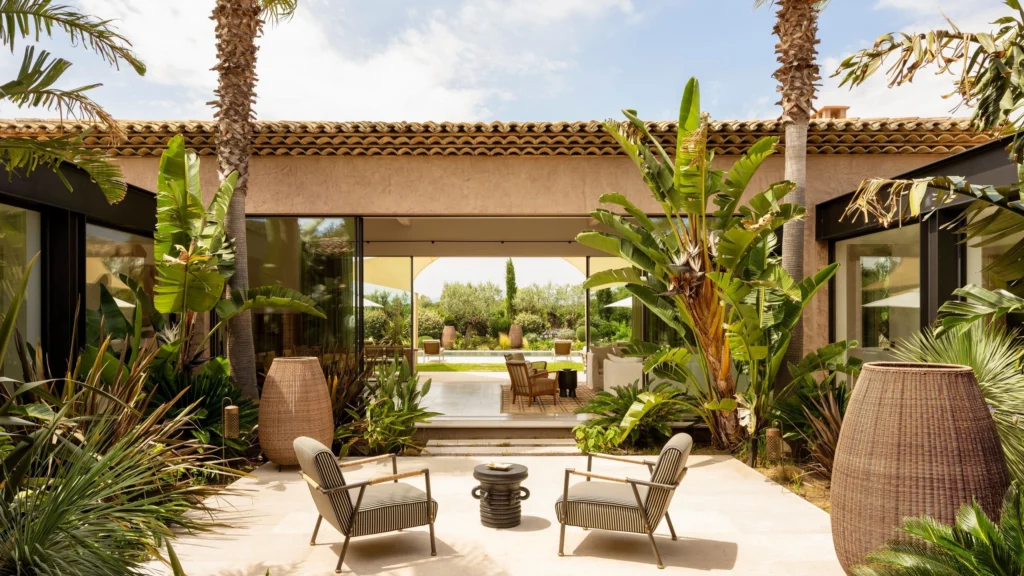 Riviera luxury home courtyard blending tropical Mediterranean landscaping with contemporary coastal modernism and understated outdoor furniture.