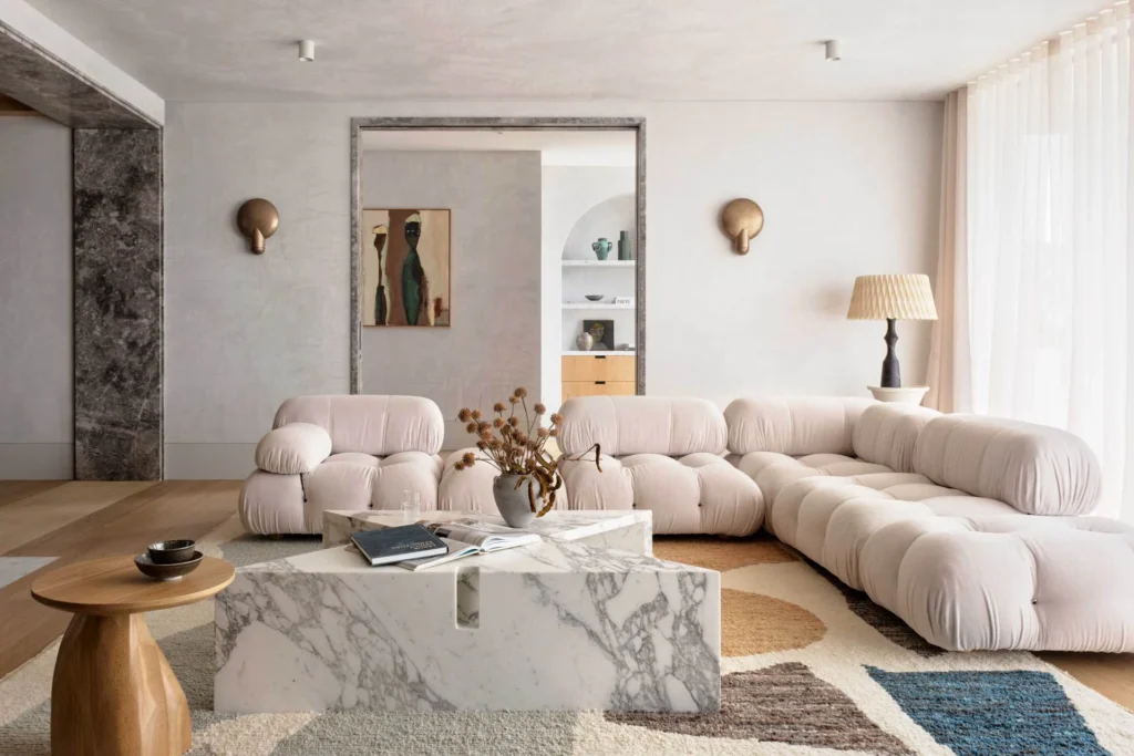 Elegant contemporary interior with a curved modular sofa, honed marble coffee table, and textured plaster walls illustrating the role of tactile design in luxury interiors.
