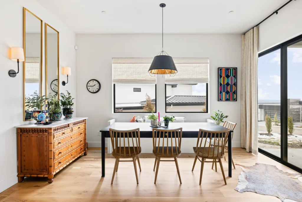 Sophisticated dining area demonstrating layered lighting design, where ambient ceiling lighting and functional pendant lights define the dining table within a warm, contemporary kitchen setting.
