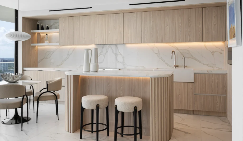 Minimalist contemporary kitchen showcasing balanced ambient lighting and functional task lighting, with integrated LED strips illuminating cabinetry and a sculptural island in light wood and marble.