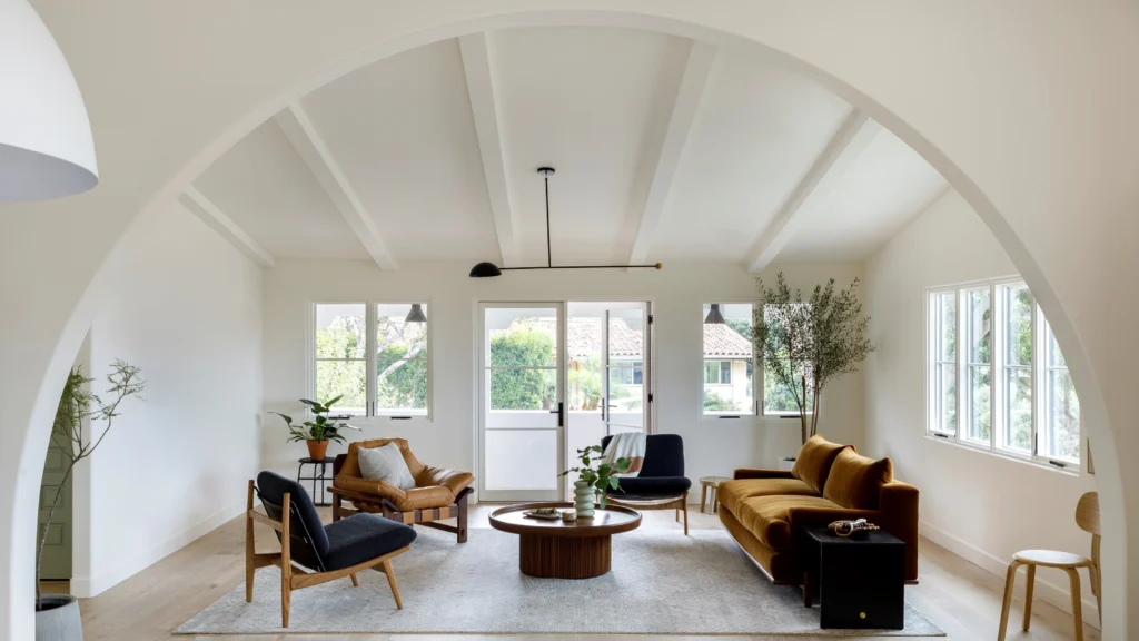 Modern open-plan living interior showcasing distinct zones defined by a floating sofa, large area rugs, statement lighting, and strategic furniture layout connecting lounge, dining, and kitchen areas with cohesive materials and natural light.