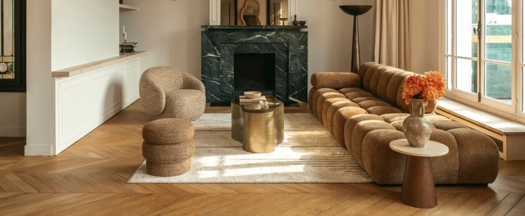 Luxurious contemporary living interiors showcasing leather and upholstered seating, including a sculptural cognac leather lounge chair with ottoman, a refined leather sofa in a light-filled space, textured bouclé armchairs, and elegant modern living rooms with marble fireplaces, brass tables, natural wood floors, and expansive floor-to-ceiling windows overlooking greenery or water.