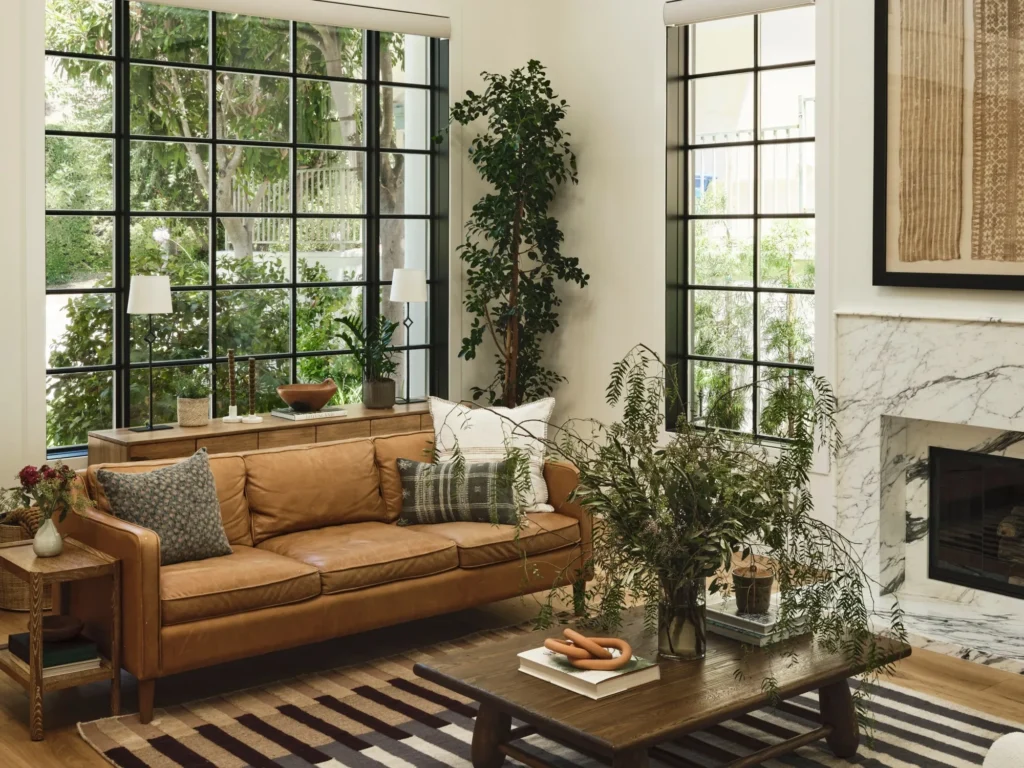 Luxurious contemporary living interiors showcasing leather and upholstered seating, including a sculptural cognac leather lounge chair with ottoman, a refined leather sofa in a light-filled space, textured bouclé armchairs, and elegant modern living rooms with marble fireplaces, brass tables, natural wood floors, and expansive floor-to-ceiling windows overlooking greenery or water.