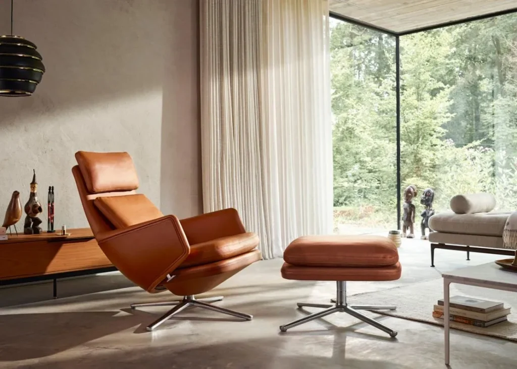 Luxurious contemporary living interiors showcasing leather and upholstered seating, including a sculptural cognac leather lounge chair with ottoman, a refined leather sofa in a light-filled space, textured bouclé armchairs, and elegant modern living rooms with marble fireplaces, brass tables, natural wood floors, and expansive floor-to-ceiling windows overlooking greenery or water.