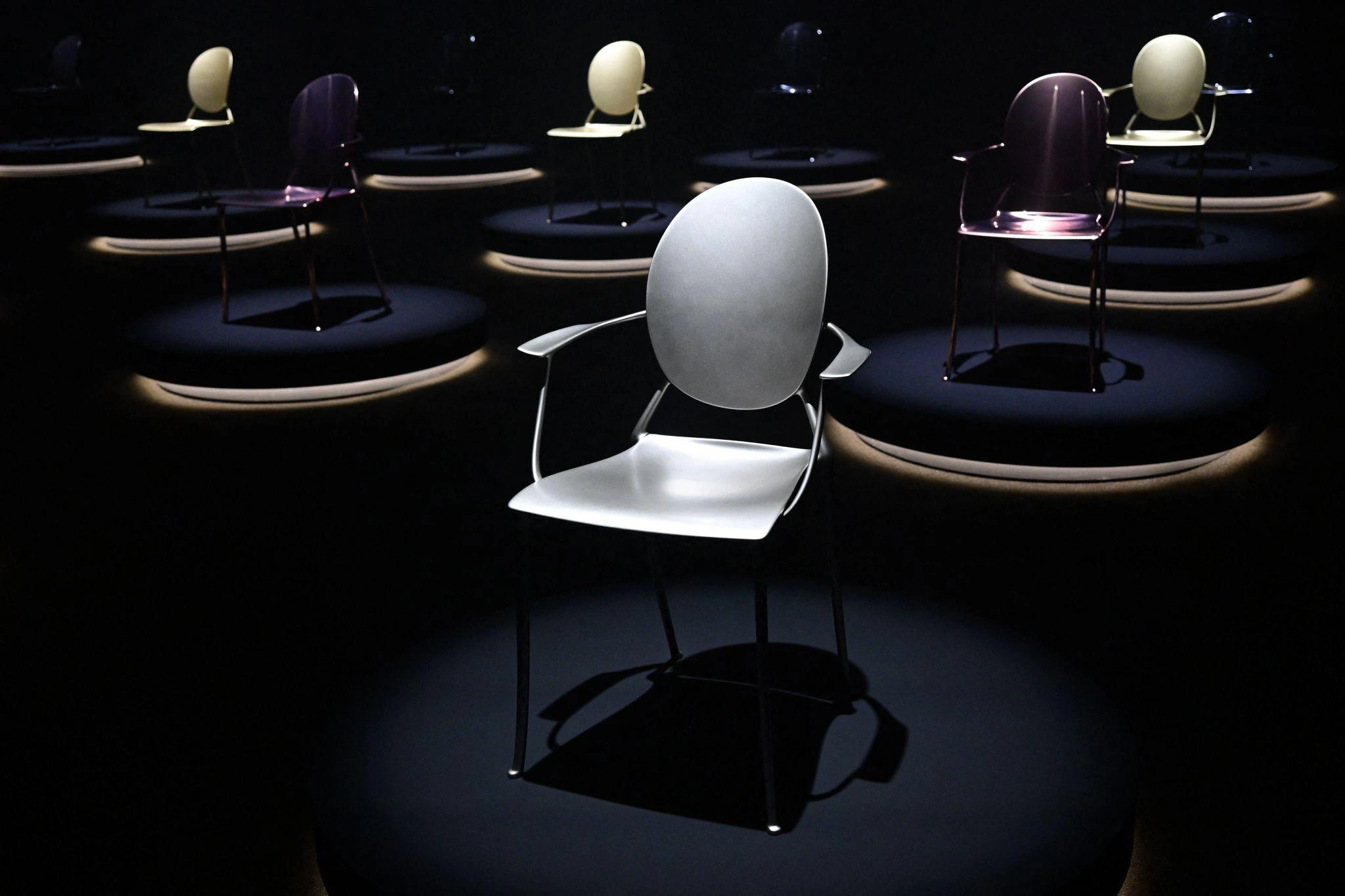 Sculptural contemporary chairs displayed on illuminated circular platforms, showcasing innovative forms and finishes at Salone del Mobile 2026.