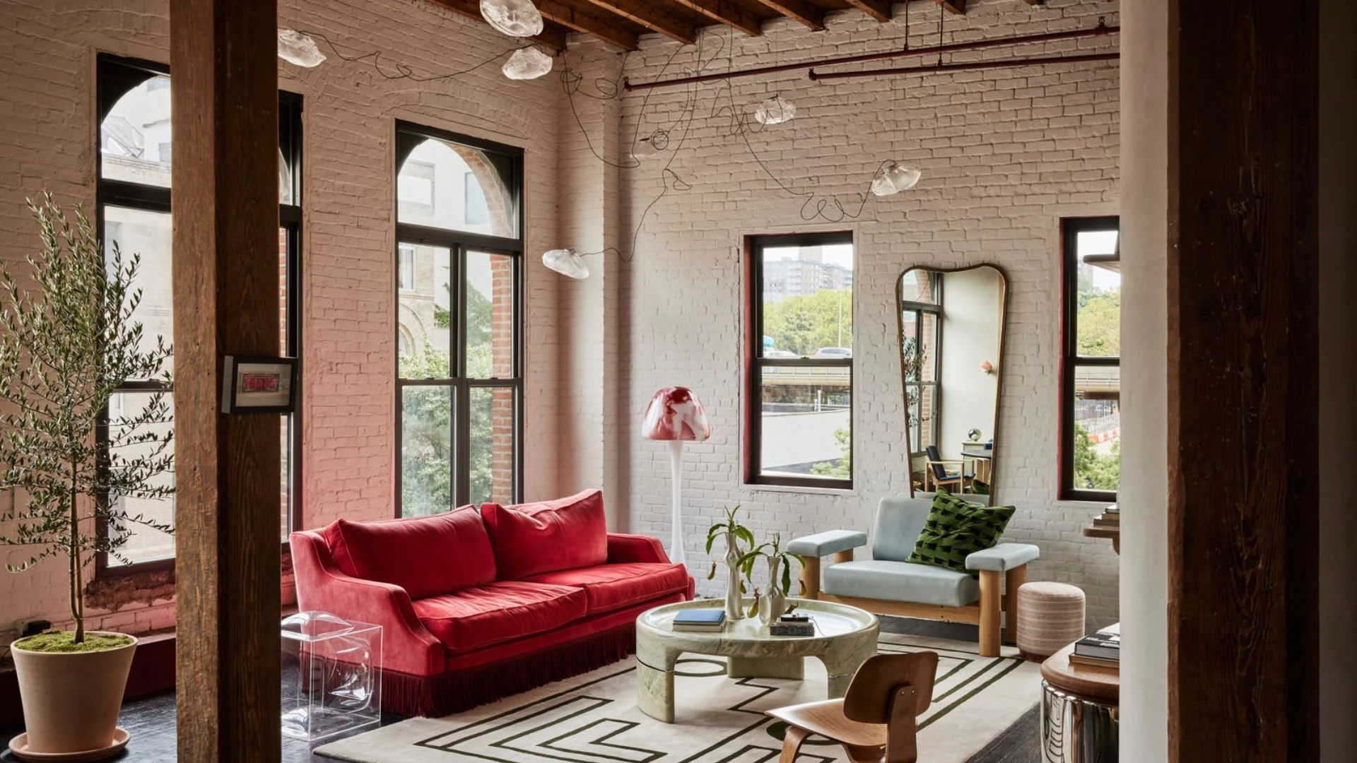 Luxury SoHo loft interior design in a historic New York loft featuring exposed brick walls, cast-iron columns, double-height industrial windows and expansive industrial loft living rooms styled with sculptural modular sofas, plush bouclé and leather seating, oversized area rugs, contemporary art, and warm ambient lighting balancing raw architecture with refined soft furnishings.